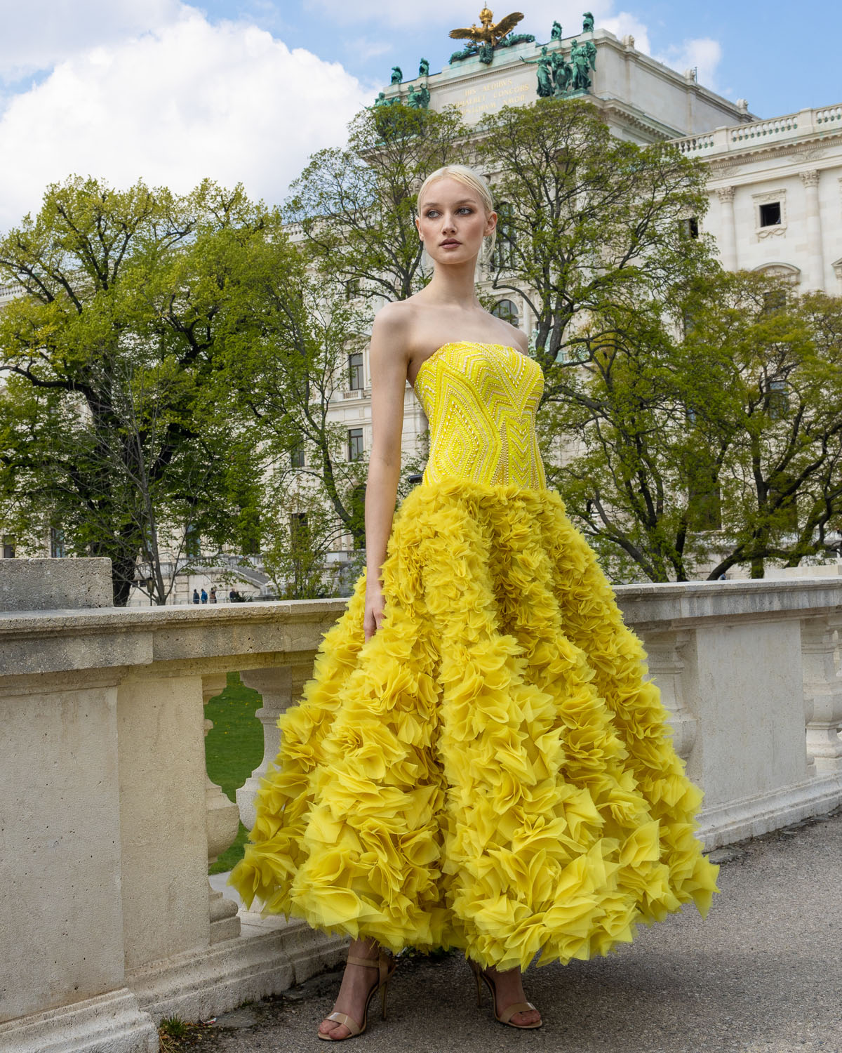 Side view of a woman in a Strapless, bright yellow gown, beaded bodice and a voluminous skirt adorned with layers of ruffled fabric. 2, image 1